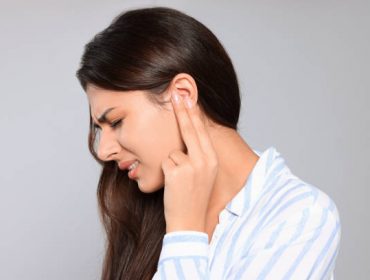 Young woman suffering from ear pain on light grey background