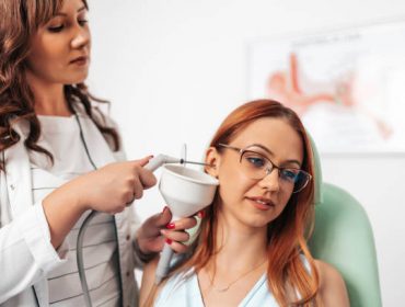 Otolaryngologist doing ear irrigation and earwax removal to a young adult woman with modern medical equipment. Healthcare and medicine concept.